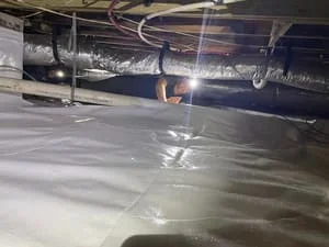 White vapor barrier membrane installed across crawl space floor with support posts visible