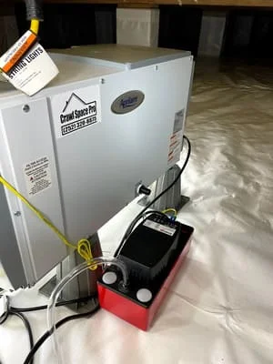Dehumidifier unit with red condensate basin installed in crawl space on plastic sheeting