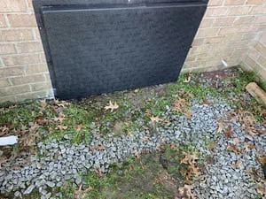 Black moisture barrier installed over gravel base against brick foundation wall
