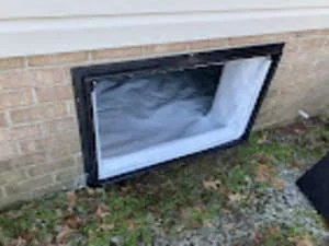 White vapor barrier installed in crawl space with black frame against brick foundation wall