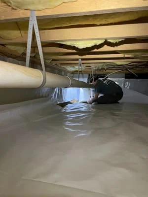 Crawl space with white vapor barrier membrane installed on floor and exposed wooden joists above