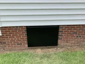 Black vapor barrier crawl space encapsulation installed on brick foundation with grass grade