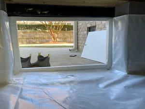 Crawl space with white vapor barrier lining floor and walls, foundation opening visible