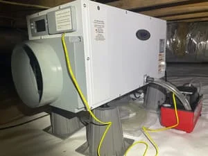 Dehumidifier unit with yellow ducting installed in crawl space foundation area