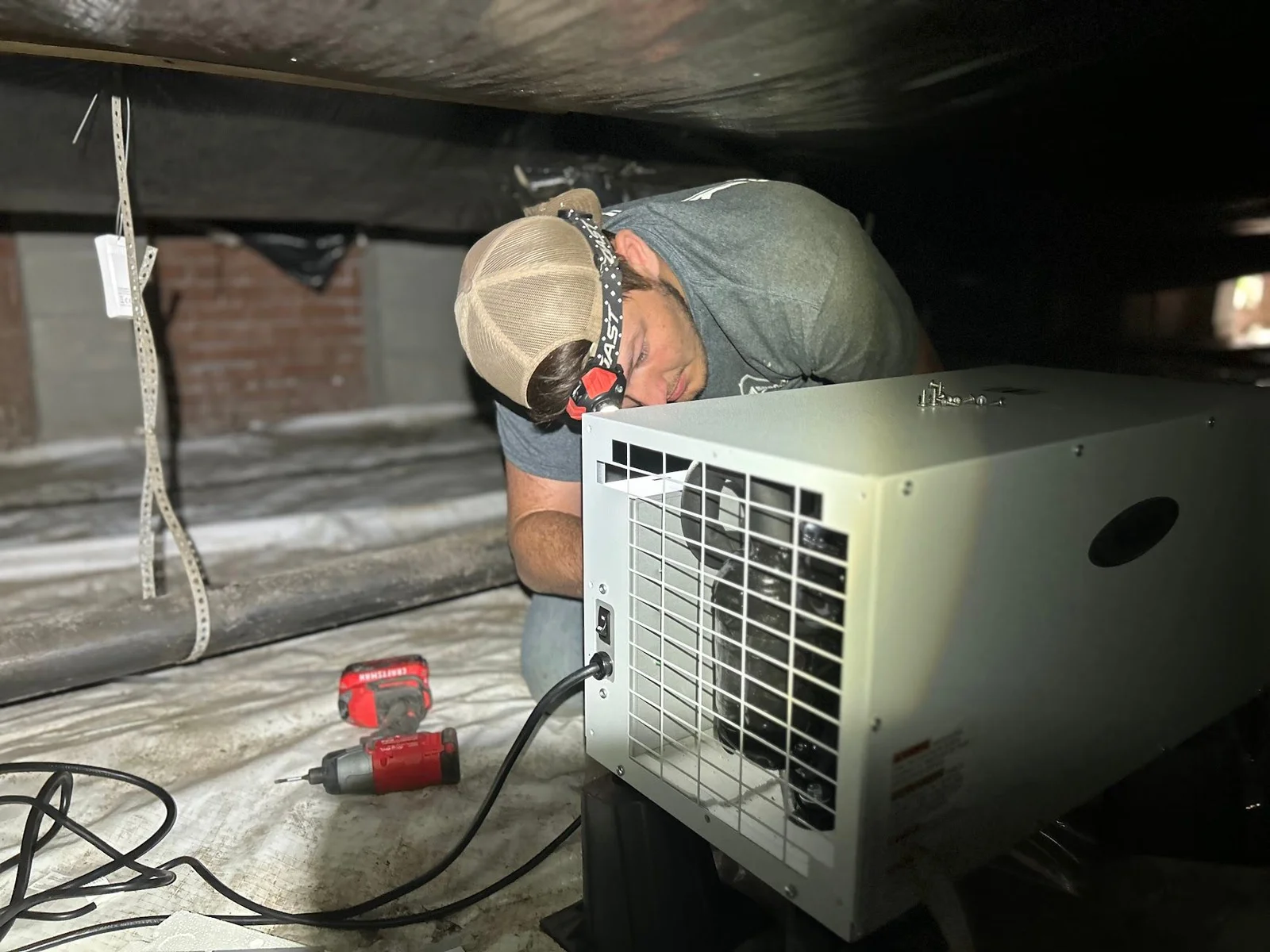 A crawl space dehumidifier installed beneath a Grimesland, NC home, with a drain line routed away from the unit and visible moisture control equipment in a low-clearance crawl space.