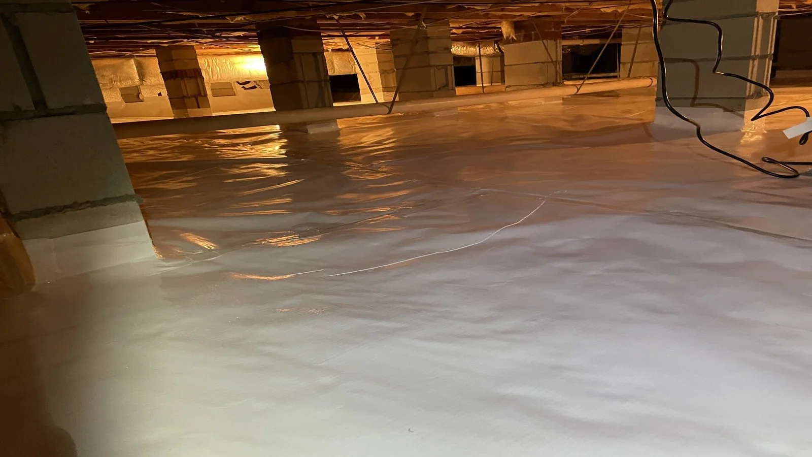 A clean plastic vapor barrier installed across the dirt floor and lower walls of a crawl space beneath a home in Grimesland, NC. The sheeting covers the ground surface fully, with overlapping seams visible along the perimeter.